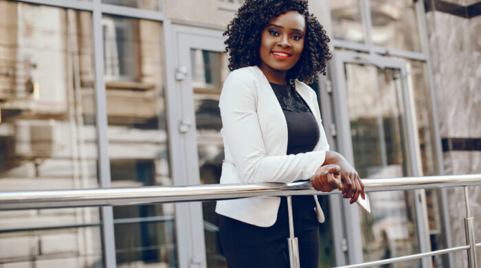 elegant and stylish dark-skinned girl with curly hair and in a white jacket standing in the summer city and using the phone