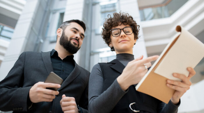 Curly-haired businesswoman in glasses pointing in clipboard while explaining development strategy to colleague