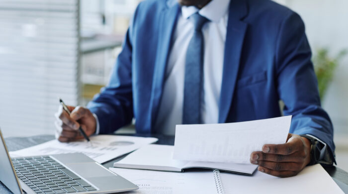 Close up of unrecognizable black businessman wearing suit analyzing data reports at workplace, copy space