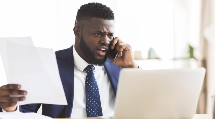 Furious general manager yelling at employees by phone Furious african american general manager yelling at employees by phone, unhappy with business report, office interior, copy space