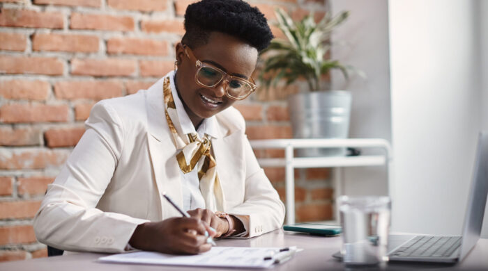 African American female CEO taking notes while working on computer in the office.