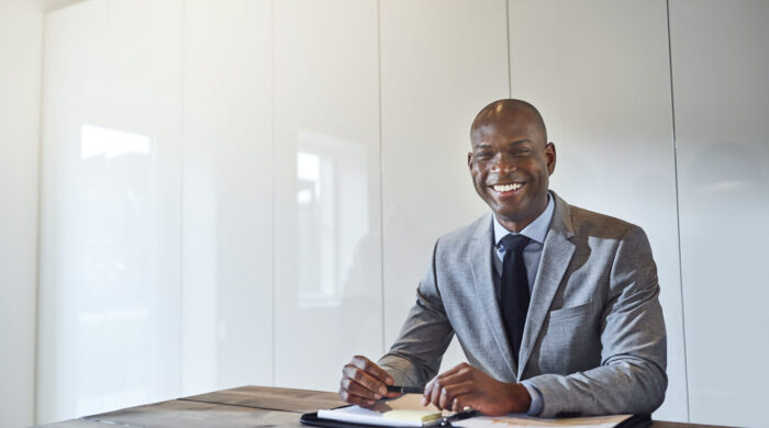 Smiling young African American businessman sitting alone at a table in a boardroom with a folder full of paperwork