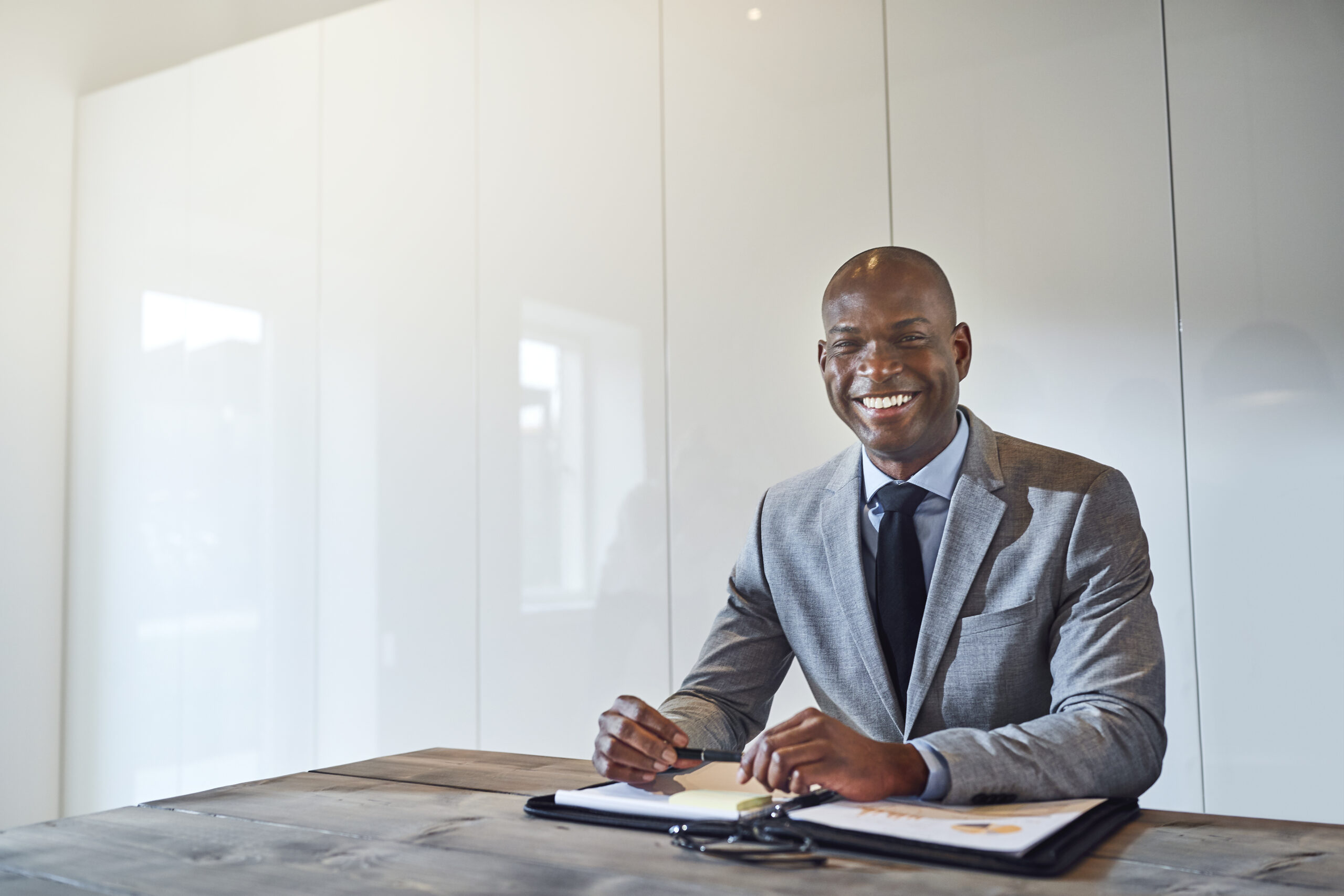 Smiling African American Businessman Sitting With Paperwork In A Boardroom