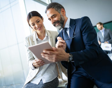 Happy business colleagues in modern office talking and using tablet