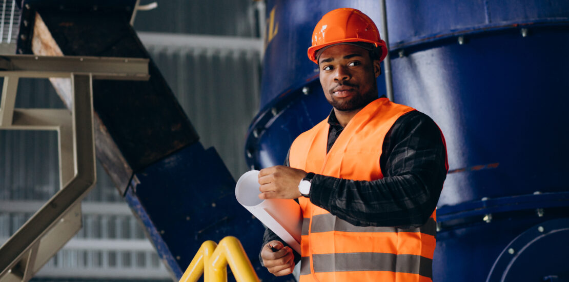 African American Worker Standing In Uniform Wearing A Safety Hat In A Factory