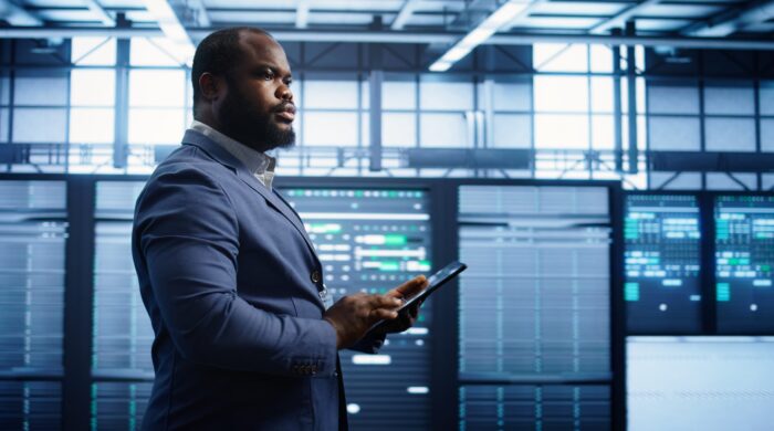 Technician walking in server room, doing checkup, inputting data on tablet of needed fixes. IT professional working in data center facility housing storage infrastructure, camera B
